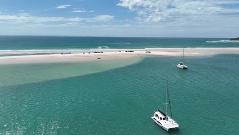 flying-over-catamaran-in-bay-towards-4x4-vehicles-parked-on-white-sandy-beach