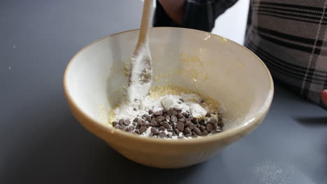 A-girl-mixing-chocolate-chips-into-cookie-dough-cake-mixture-in-a-bowl-with-a-wooden-spoon