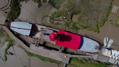 Aerial-view-above-a-lightship-stuck-in-mud-at-low-tide,-sunny-Tollesbury,-UK---screwdriver,-drone-shot