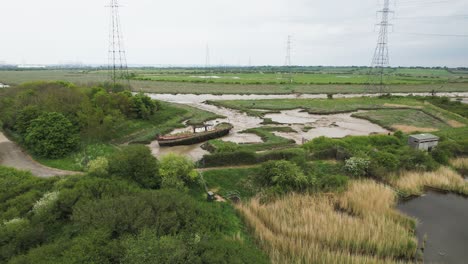Wat-Tyler-eroded-marshland-with-decaying-abandoned-fishing-boat-moored-on-riverbanks-orbiting-aerial-view