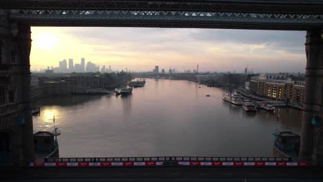 Sensational-aerial-view-of-Tower-Bridge-in-London,-drone-flying-backwards-at-pink-sunset-sky,-rises-reveals-UK's-capital-cityscape
