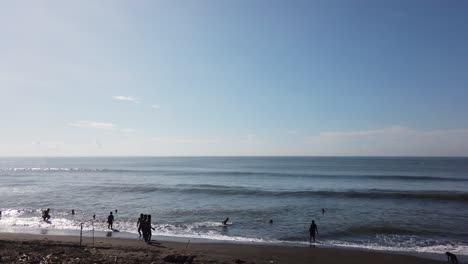 People-Swimming-and-Bathing-in-the-Black-Sand-Beach-Sea,-Bali,-Indonesia-Ketewel-60-Fps-Clear-Blue-Open-Sky-Panorama