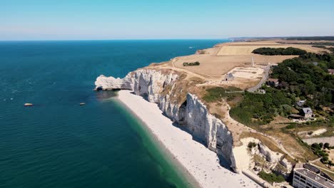 Aerial-panoramic-shot-of-famous-cliffs-with-sandy-beach-and-blue-sea-in-Etretat,France---Agricultural-fields-in-background-at-sunlight
