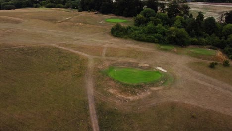Aerial-high-shot-over-a-golf-course-hole-on-a-green,-camera-tilting-in-Royston,-Hertfordshire,-England,-Uk