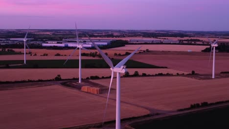 Aerial-Moving-down-wind-turbines-farm-during-blue-hour,-pink-sunset-over-fields-in-Langford,-Biggleswade,-Bedfordshire,-England,-Uk
