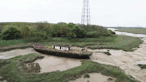 Flying-over-Wat-Tyler-abandoned-moss-covered-fishing-trawler-moored-in-muddy-riverbank