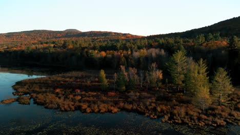 Sunset-aerial-over-lake-next-to-mountain-forest-in-stunning-autumn-colours