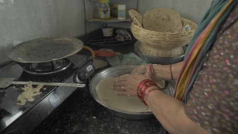 Side-angle-close-up-shot-of-a-senior-aged-woman-making-traditional-bhakri-in-Indian-kitchen-using-cooking-gas-stove