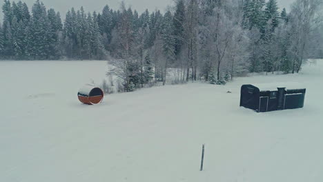 Slow-and-steady-tracking-in-shot-of-wooden-cabin-and-sauna-surrounded-by-trees-in-the-middle-of-nowhere-with-freshly-covered-snow