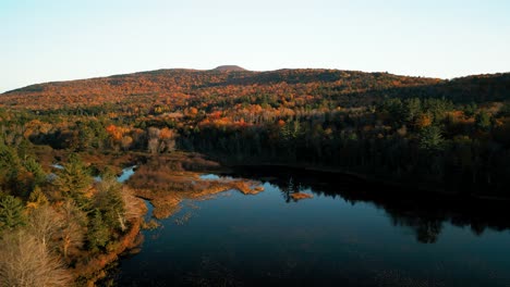Beautiful-wilderness-scene-in-Catskill-Mountains---aerial-over-lake-with-forest-on-slopes-in-fall-foliage