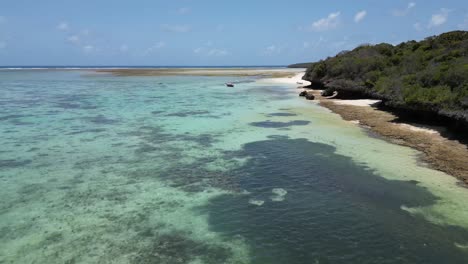 Shallow-coral-lagoon-in-Pungume-Island-Tanzania-Africa-southern-Zanzibar-with-sailboat-anchored,-Aerial-dolly-in-low-shot