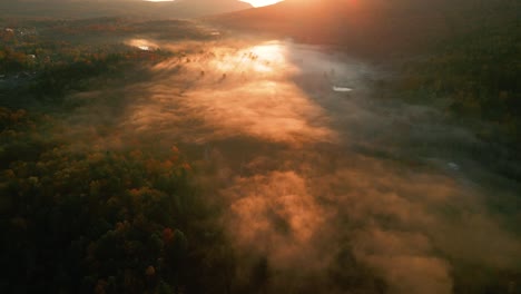 Dense-fog-lying-over-lake-at-dreamy-sunrise,-fall-in-Catskill-Mountains,-aerial