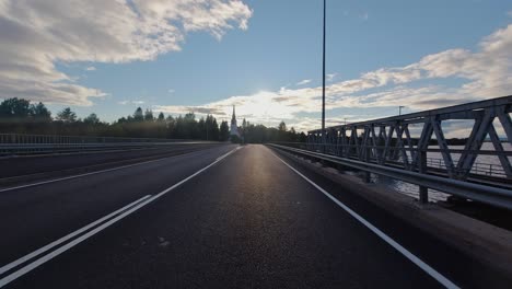 Vehicle-POV:-Driving-on-bridge-directly-into-morning-sunrise,-steeple