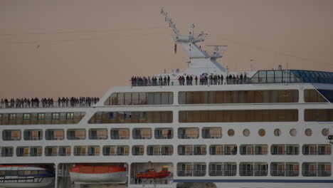 Passengers-Standing-Along-Top-Deck-Of-Cruise-Ship-During-Golden-Hour