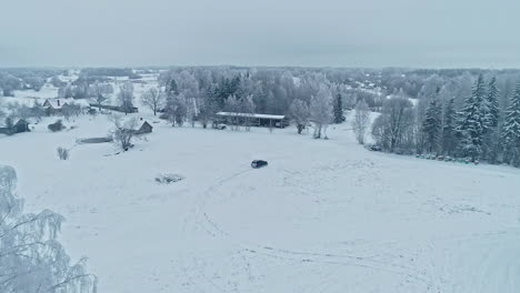 Aerial-drone-forward-moving-shot-over-a-black-car-parked-surrounded-by-white-snow-covered-during-cold-winter-day