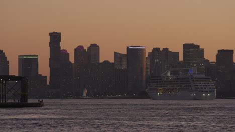 Passenger-Cruise-Ship-Passing-New-Jersey-Cityscape-Against-Orange-Sunset-Sky-On-The-River-Hudson