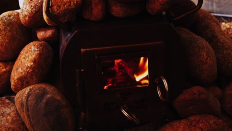 Orange-flames-blaze-in-cozy-wood-stove-surrounded-by-hot-rocks