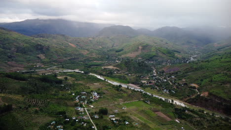 Iconic-Vietnam-village-near-river-and-massive-mountains,-high-altitude-aerial