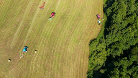 Aerial-drone-bird's-eye-view-over-tractors-ploughing-through-large-farmland-on-a-bright-sunny-day