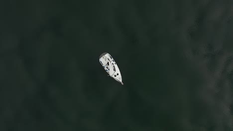 Von-Oben-Nach-Unten-Aufsteigende-Drohnenaufnahme---Segelboot-Auf-Ruhigem-See-Mit-Wolkenreflexion-Auf-Wasserfläche
