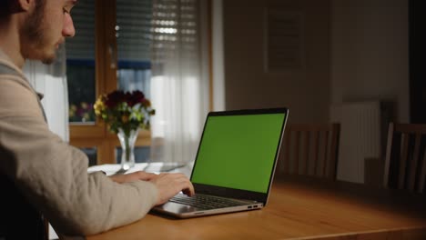 Jemand-Tippt-Auf-Dem-Laptop-Mit-Grünem-Bildschirm-Im-Wohnzimmer,-Mit-Licht-Von-Außen