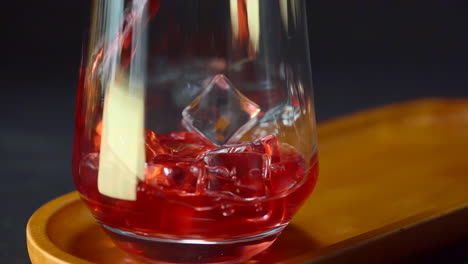 Pouring-red-liquid-into-transparent-glass-cup-with-ice-cubes