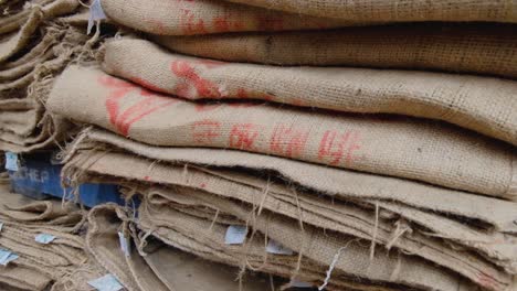 Stacks-of-used-natural-hessian-jute-coffee-sacks-in-a-coffee-production-warehouse-to-store-coffee-beans-for-distribution
