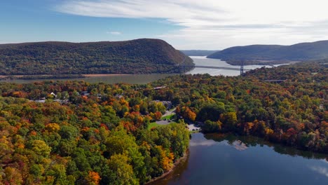 An-aerial-view-over-a-reflective-lake-with-colorful-trees-in-autumn,-upstate-NY