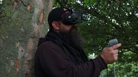 Bearded-male-wearing-virtual-FPV-goggles-controlling-drone-in-park-with-motion-joystick