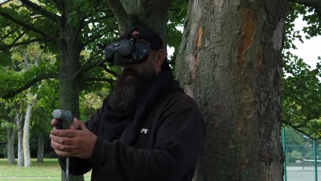 Bearded-male-wearing-FPV-goggles-controlling-drone-in-park-with-motion-controller-joystick