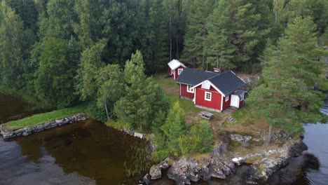 Slow-zoom-out-of-a-typical-old-swedish-red-cabin-in-the-at-a-lake-surrounded-by-pine-trees-and-a-dark-lake