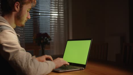 Jemand-Tippt-Auf-Dem-Laptop-Mit-Grünem-Bildschirm-Im-Wohnzimmer-Mit-Nebel-Und-Licht-Von-Außen