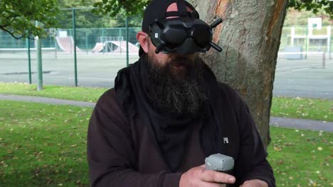 Bearded-man-wearing-FPV-goggles-controlling-drone-in-park-with-motion-joystick