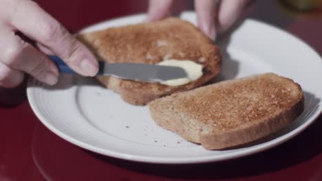 hands-of-a-caucasian-model-while-smearing-butter-on-a-toast---slow-motion,-close-up