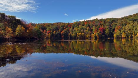 A-low-angle,-aerial-view-of-a-reflective-lake-with-colorful-trees,-during-the-fall-foliage-in-upstate-NY