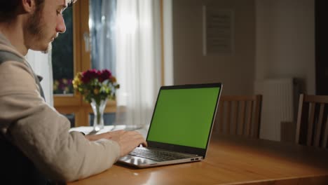 Jemand-Tippt-Auf-Dem-Laptop-Mit-Grünem-Bildschirm-Im-Wohnzimmer,-Mit-Licht-Von-Außen