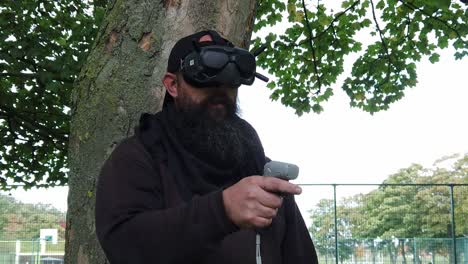 Bearded-male-wearing-FPV-goggles-controlling-drone-in-park-with-motion-joystick