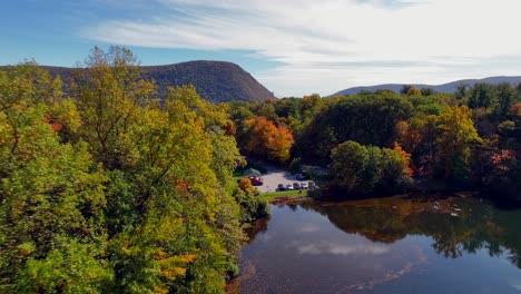 An-aerial-view-over-a-reflective-lake,-surrounded-by-colorful-trees-during-the-fall-foliage-in-upstate-NY