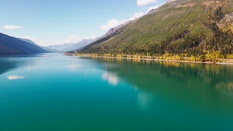 truck-right-hyperlapse-aerial-wide-shot-of-moose-lake-in-Mount-Robson-Provincial-Park-in-autumn-with-yellow-trees-and-mountains-in-the-background-and-cars-driving-on-the-highway-with-green-blue-water