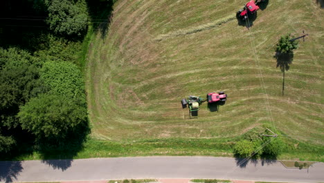 Aerial-view-looking-down-at-pair-of-diesel-tractors-gathering-and-forming-bales-on-agricultural-farmland