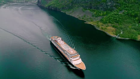 Aerial-drone-bird's-eye-view-over-giant-cruise-ship-in-motion-along-Norwegian-Fjord-in-Flam,-Norway-on-a-cloudy-day