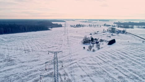 Aerial-backwards-shot-snowy-winter-landscape-with-electric-transmission-towers-during-purple-sky-in-the-morning