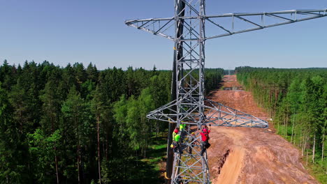 Drone-shot-of-worker-climbing-and-build-new-electricity-pylon-in-forest-woodland-during-sunny-day