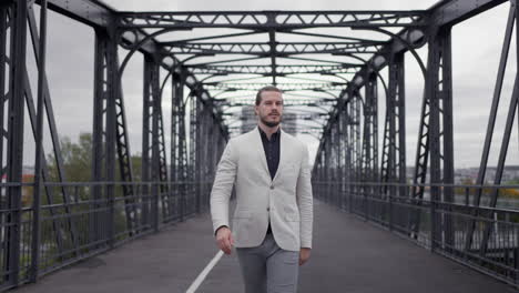 Confident-adult-businessman-in-formal-suit-walking-through-the-bridge-at-the-morning