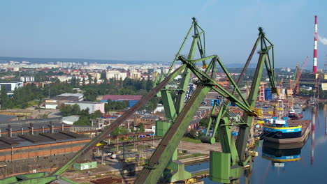 Drone-shot-of-old-Container-harbor-with-rusty-cranes-in-Gdansk,Poland-during-sunny-day---Cityscape-in-background