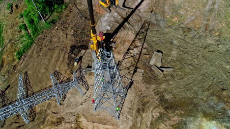 Aerial-top-down-shot-of-worker-on-build-new-transmission-tower-on-field-during-sunny-day---tracking-shot