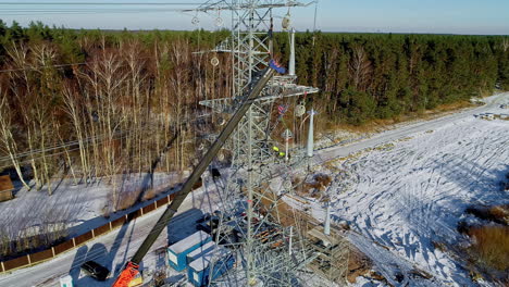 Aerial-view-of-worker-working-on-transmission-tower-in-forest-during-snowy-winter-day