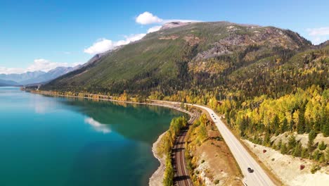 pan-right-aerial-wide-shot-of-Yellowhead-Highway-along-moose-lake-in-Mount-Robson-Provincial-Park-in-autumn-with-yellow-trees-and-mountains-in-the-background-and-cars-driving-on-the-highway
