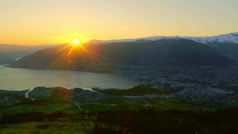 Aerial-drone-backward-moving-shot-over-of-typical-Norwegian-village-beside-fjord-shores-in-Norway-as-sun-rising-from-behind-mountains