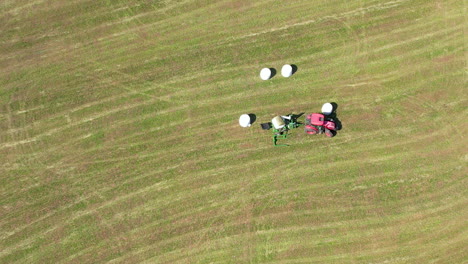 Aerial-straight-down-shot-of-tractor-transporting-fresh-hay-bales-on-grass-field-in-summer